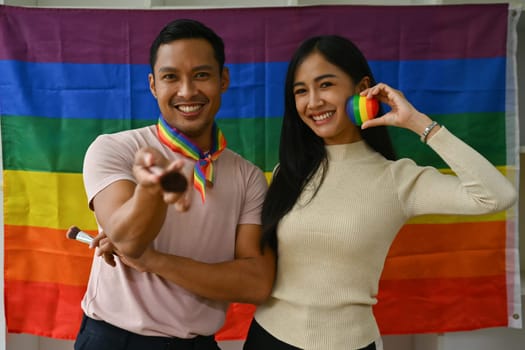 Beauty blogger and trans gender influencer standing against LGBTQ rainbow flag and smiling to camera.