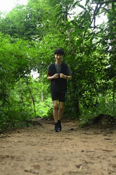 Full length of sporty man in sportswear running in woods on trail. Sports, adventure and healthy lifestyle.