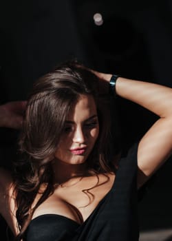 Portrait of a sexy brunette in a black dress on a dark background. girl takes off her dress slowly in the bedroom.