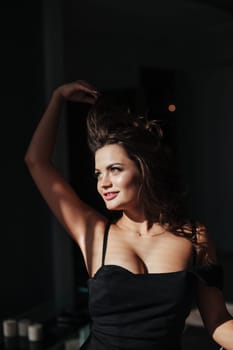 Portrait of a sexy brunette in a black dress on a dark background. girl takes off her dress slowly in the bedroom.