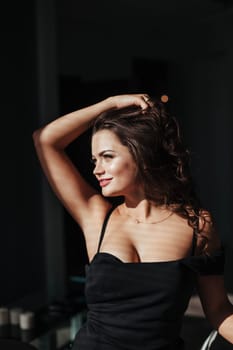 Portrait of a sexy brunette in a black dress on a dark background. girl takes off her dress slowly in the bedroom.