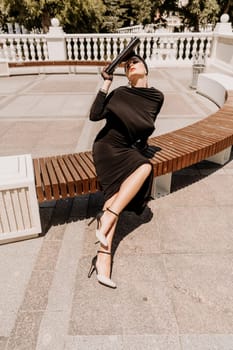 Stylish woman in the city. Fashion photo of a beautiful model in an elegant black dress posing against the backdrop of a building on a city street.