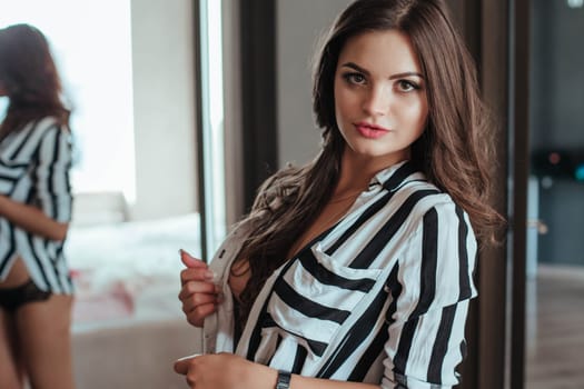 Seductive woman portrait of trendy woman in shirt and lingerie on bed. Stylish fashion girl model posing in mirror in bedroom.