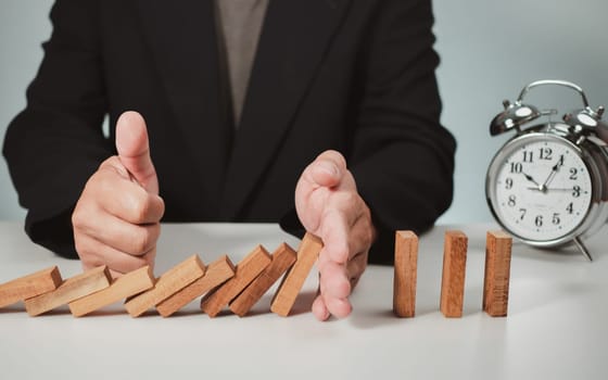 Risk management concept. Businessman hand stopping dominoes effect for business. 