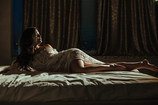 Sexy girl in a transparent tunic on the bed. underwear on a graceful body in the night light of a warm lamp. tempting a man on Valentine's Day.