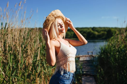 Beautiful model girl posing on the field enjoying nature outdoors in a straw hat. Beauty blond young woman with long straight blond hair close up portrait.