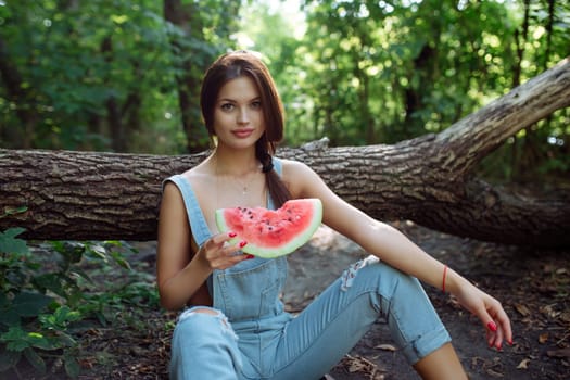 Picnic in nature and healthy eating. A sexy girl in the woods eats watermelon. Portrait of a woman with a berry in her hands.