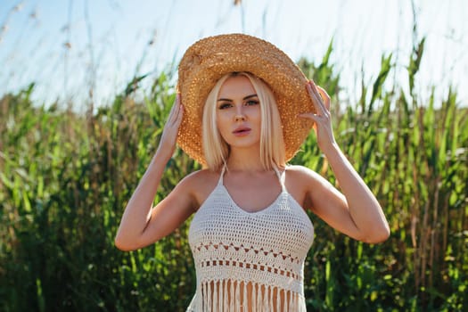 Beautiful model girl posing on the field enjoying nature outdoors in a straw hat. Beauty blond young woman with long straight blond hair close up portrait.