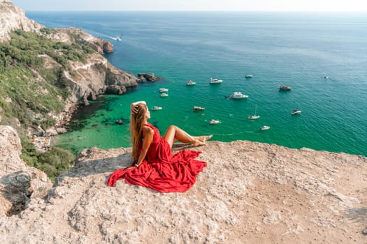 Woman sea red dress yachts. A beautiful woman in a red dress poses on a cliff overlooking the sea on a sunny day. Boats and yachts dot the background