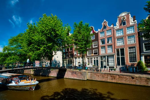 AMSTERDAM, NETHERLANDS - MAY 21: Amsterdam canal with tourist boat passing under bridge and old houses. Amsterda, Netherlands