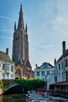 Bruges, Belgium - May 28, 2018: Tourist boat in canal near Church of Our Lady . Brugge Bruges, Belgium