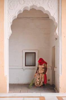 Jodhpur, India - November 13, 2019: Woman in traditional indian Rajasthani clothes sweeping and cleaning the ground with broom in Mehrangarh fort. Jodhpur, Rajasthan, India
