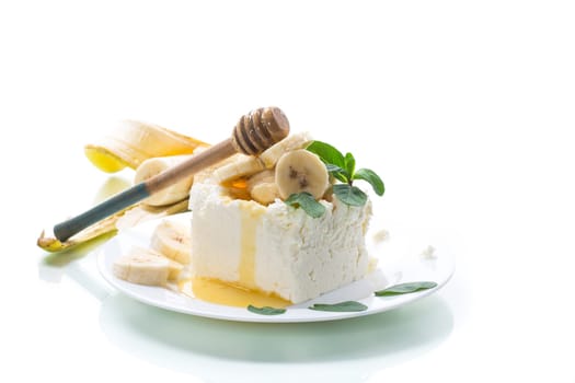 Portion of homemade milk curd with banana slices and honey, isolated on white background.