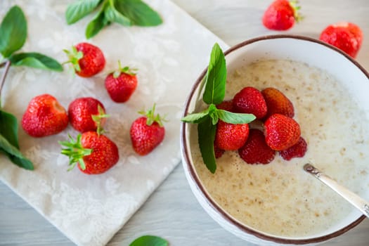 cooked diet oatmeal in a bowl with fresh ripe strawberries, on a wooden table.