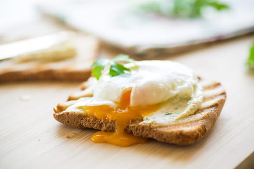 Fried toast bread with spread and poached egg, on a wooden table. Quick breakfast.