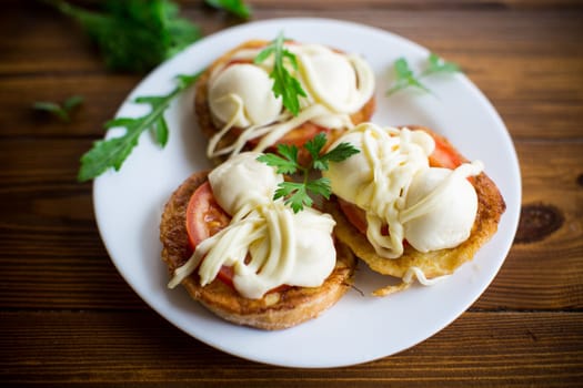 fried in batter sandwiches with tomatoes and mozzarella in a plate with herbs, on a wooden table.