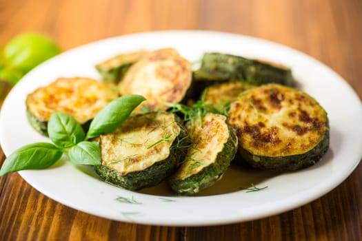 zucchini fried in circles with spices and herbs, in a plate on a wooden table.