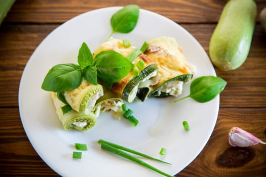 cooked zucchini rolls with cheese filling inside, in a plate on a wooden table