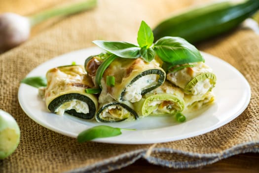 cooked zucchini rolls with cheese filling inside, in a plate on a wooden table