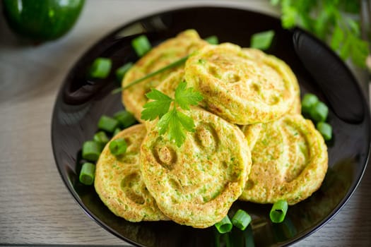 Fried squash green pancakes in a plate, on a wooden table.