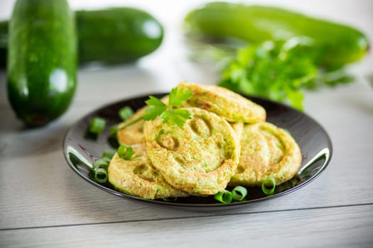 Fried squash green pancakes in a plate, on a wooden table.
