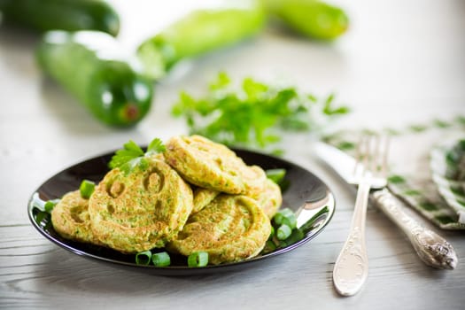 Fried squash green pancakes in a plate, on a wooden table.