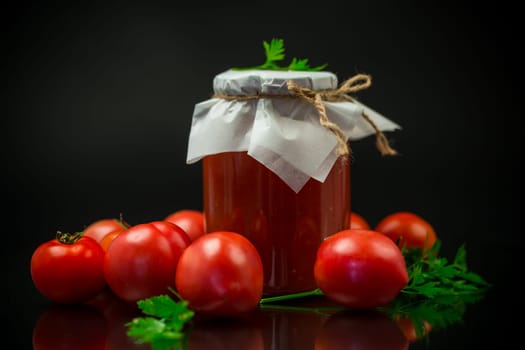 Cooked homemade tomato juice canned in a jar of natural tomatoes, isolated on black background.