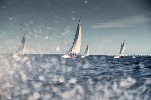 Russia, St.Petersburg, 07 July 2023: The sailing race, few boats in a roll go at high speed, sailing boats are in regatta at sunset, handsome sailors on the board of yacht, wind and splashes. High quality photo