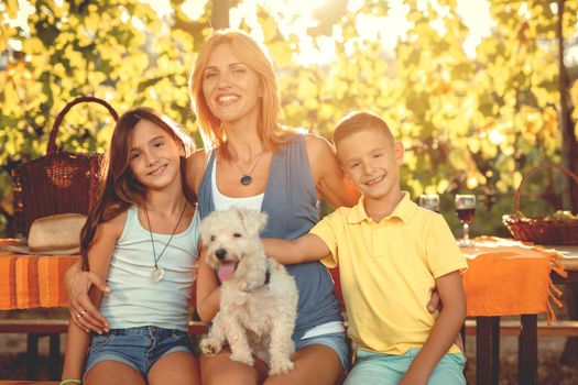 Beautiful young smiling mother with her children and their dog having picnic at a vineyard.