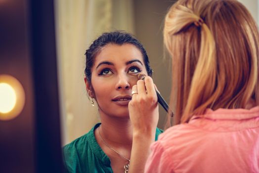 Makeup artist contouring beautiful girl's face with makeup brush. 