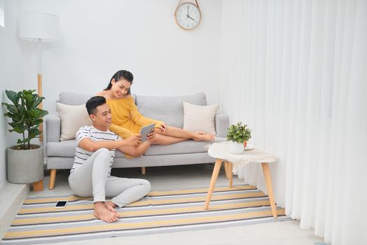 Young asian couple sitting on couch at home, using a tablet PC for Internet and social media. 