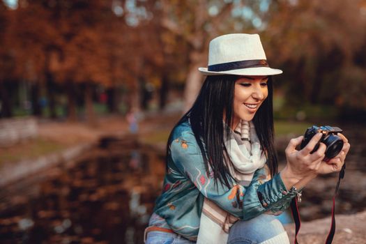 Happy woman photographer holding professional digital camera and taking photo near the lake in autumn park.  