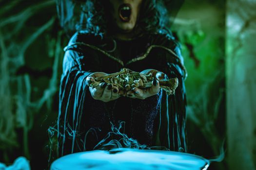 Close-up of a witches hands holding bones above boiling water for a cooking poison soup.