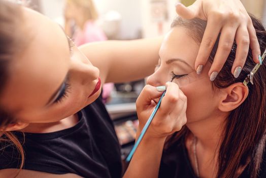 Make-up artist applying the eyeliner to model. Close-up. 