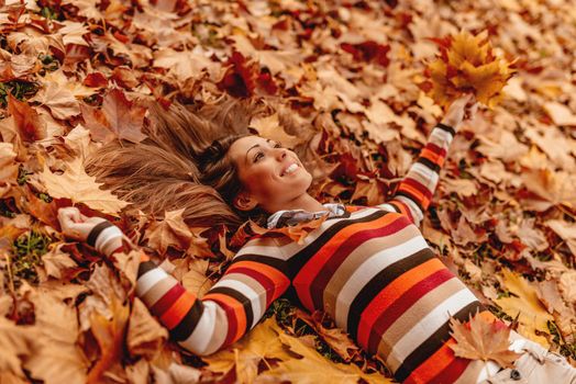 Beautiful young woman in sunny forest in autumn colors. She is lying on the fall meadow and enjoying.