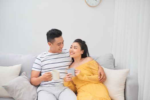 Couple in love enjoying their free time, sitting on a couch,drinking coffee and chatting.