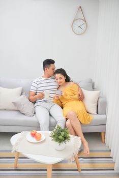 Affectionate couple holding coffee cups sitting on a sofa in the living room at home