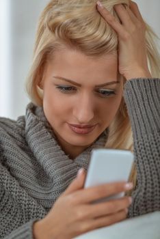 Young beautiful blonde girl with disappointment looking in a mobile phone which she is holding. 