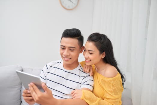 Happy young couple sitting on sofa and using digital tablet. Online shopping concept.