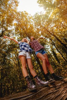 Beautiful young girls having fun in the forest. There are walking over fallen tree with arms outstretched .