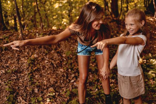Beautiful young mother and her daughter walking through forest, pointing with their fingers far away.