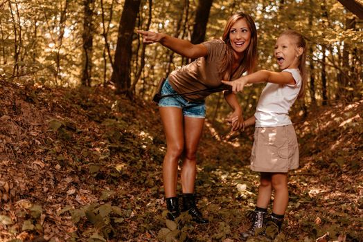 Beautiful young mother and her daughter walking through forest, pointing with their fingers far away.