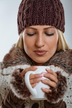 Portrait of young beautiful girl in winter clothes, blowing into a cup of tea in her hands.