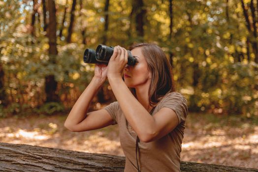 Beautiful young woman walking through forest and exploring thru binoculars.