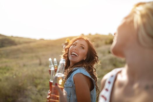 Happy young women are drinking the beer and laughing in the sunset outdoor.