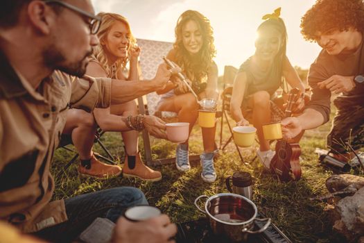 Happy young friends enjoy a sunny day in nature. They're cooking tea, laughing and talking happy to be together.