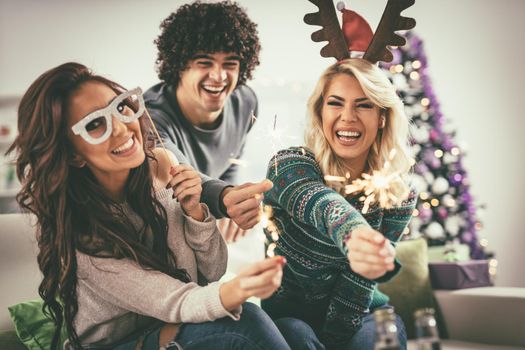 Cheerful friends having fun with sparkles in the apartment  in casual clothes.