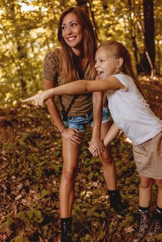 Beautiful young mother and her daughter walking through forest. Daughter is pointing with finger far away.