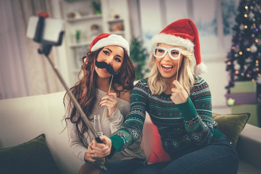 Funny female friends having nice time taking selfie in an apartment. 