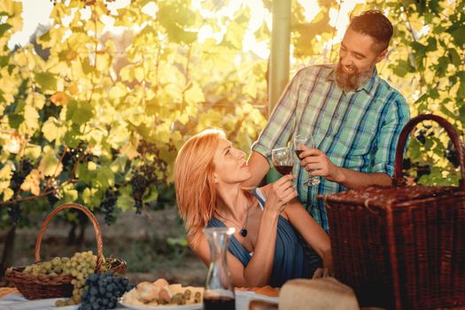Beautiful smiling couple having picnic and tasting wine at a vineyard.